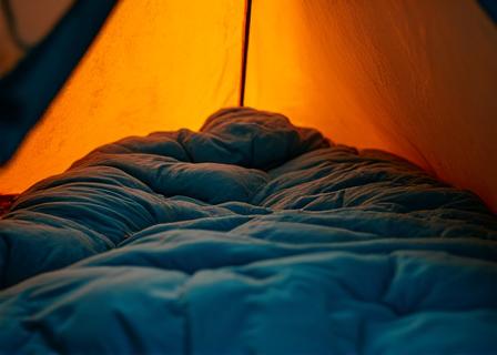 Cozy sleeping bag unrolled inside a tent, with a subtle glow, suggesting warmth